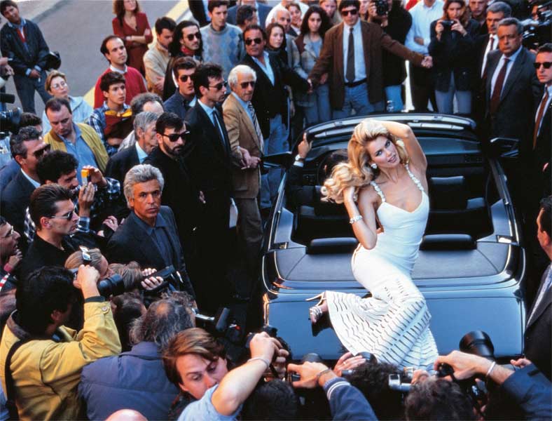 Boutique. Printemps-été 1995. Longue robe en crêpe blanc. Broderie ajourée en chevron et longs pans transparents sur les hanches. Claudia Schiffer. ©Arthur Elgort